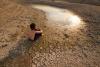 Image of a child sit on cracked earth near drying water, showing water crisis.